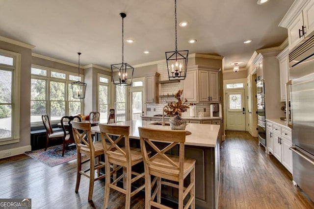 kitchen with light countertops, appliances with stainless steel finishes, backsplash, dark wood-style floors, and a center island with sink