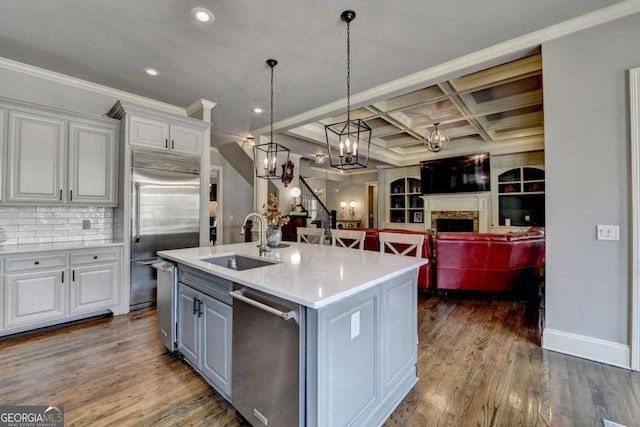 kitchen with dark wood finished floors, coffered ceiling, appliances with stainless steel finishes, a fireplace, and a sink