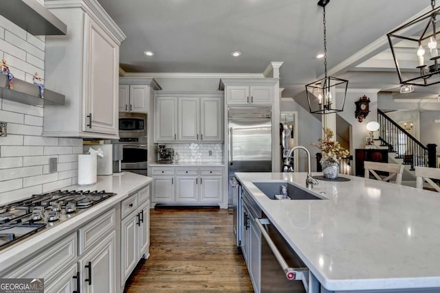 kitchen featuring dark wood-style floors, decorative light fixtures, built in appliances, a kitchen island with sink, and a sink