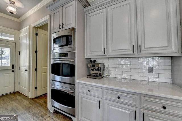 kitchen with ornamental molding, wood finished floors, appliances with stainless steel finishes, and tasteful backsplash