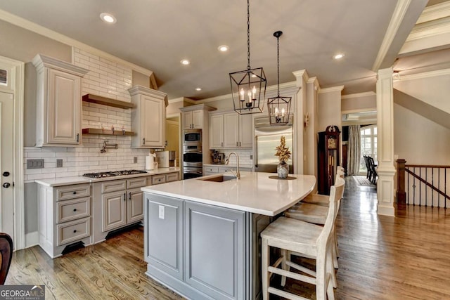 kitchen with built in appliances, a kitchen island with sink, light countertops, light wood-type flooring, and a sink