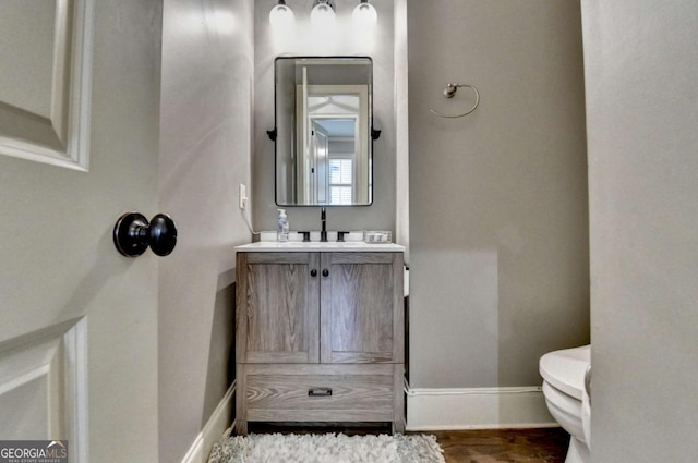 bathroom with wood finished floors, vanity, toilet, and baseboards