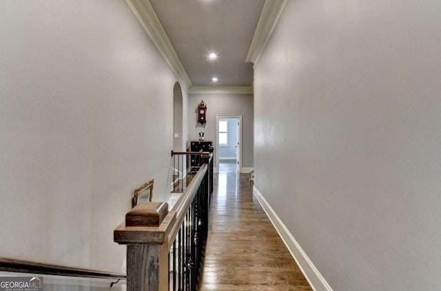 corridor with arched walkways, wood finished floors, an upstairs landing, baseboards, and ornamental molding