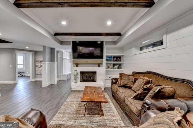 living area with baseboards, a raised ceiling, wood finished floors, a brick fireplace, and recessed lighting