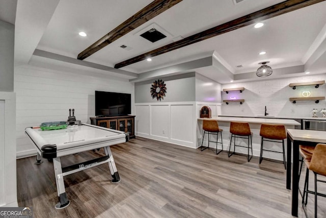 rec room featuring a wainscoted wall, visible vents, beam ceiling, wet bar, and light wood finished floors