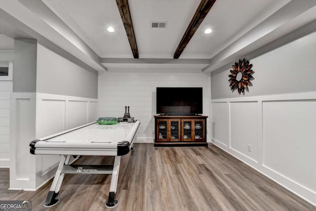 recreation room featuring visible vents, a decorative wall, beam ceiling, and wood finished floors