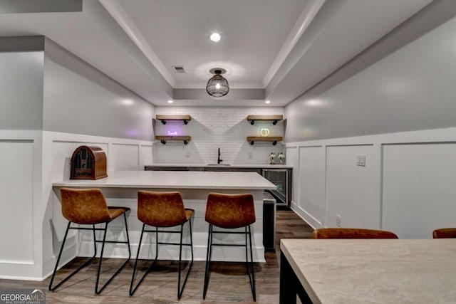 bar with a tray ceiling, indoor wet bar, a decorative wall, dark wood-type flooring, and a sink