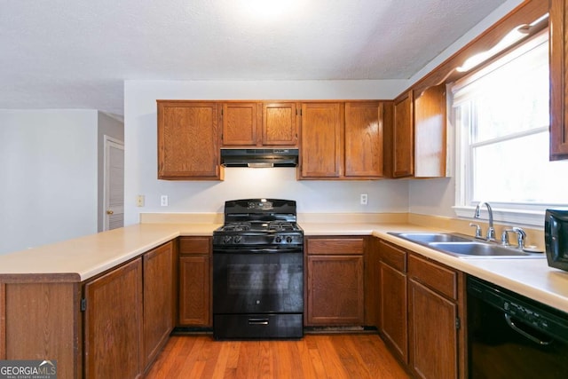 kitchen with light countertops, a sink, a peninsula, under cabinet range hood, and black appliances