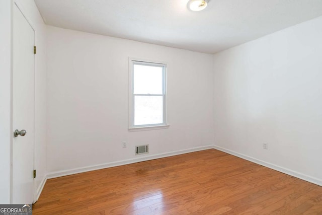 spare room with light wood-type flooring, visible vents, and baseboards