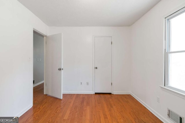 unfurnished room featuring light wood-type flooring, a healthy amount of sunlight, visible vents, and baseboards