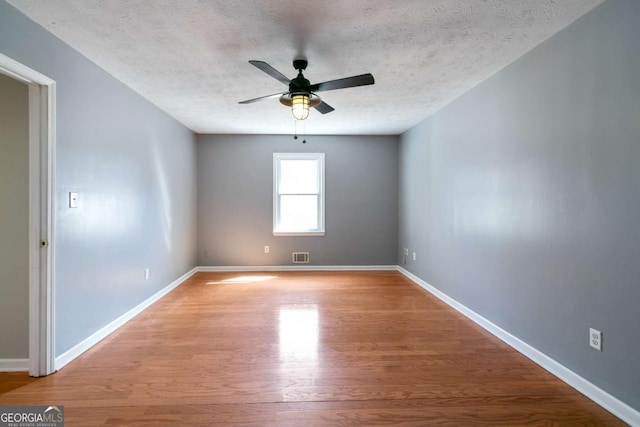 spare room with light wood finished floors, baseboards, visible vents, and a textured ceiling