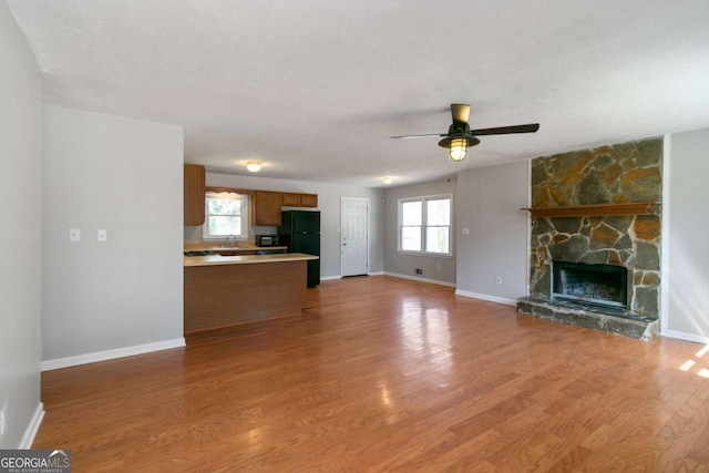 unfurnished living room with baseboards, light wood-style flooring, ceiling fan, a stone fireplace, and a sink