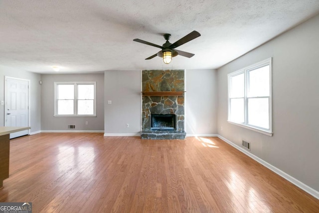 unfurnished living room with visible vents, a stone fireplace, a textured ceiling, and wood finished floors