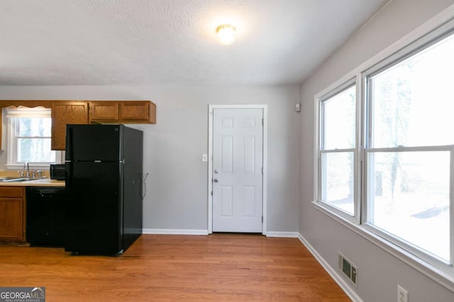 kitchen with light wood finished floors, visible vents, brown cabinetry, a sink, and black appliances