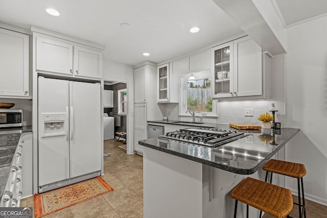 kitchen with a peninsula, white cabinets, appliances with stainless steel finishes, dark stone counters, and glass insert cabinets