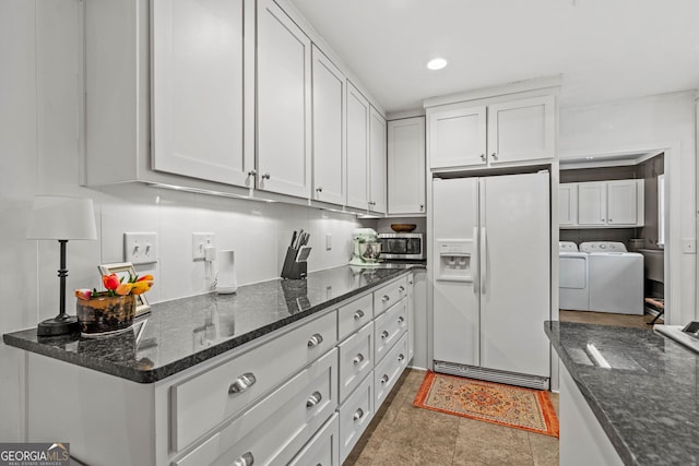 kitchen with white fridge with ice dispenser, stainless steel microwave, washing machine and clothes dryer, and white cabinetry