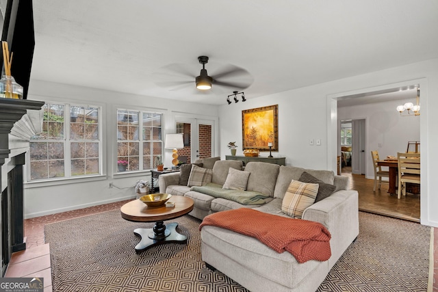 living room with a fireplace, baseboards, french doors, and ceiling fan with notable chandelier