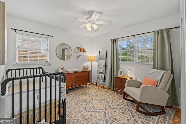 bedroom with a nursery area, ceiling fan, and baseboards