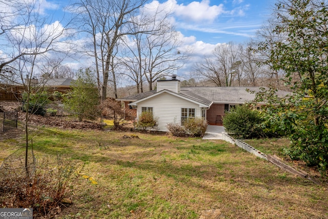 view of front facade featuring brick siding, a chimney, a front yard, and fence