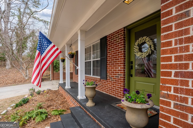 view of exterior entry with brick siding and a porch