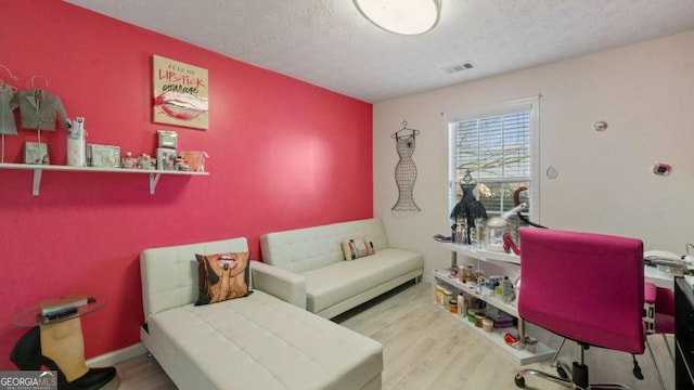 office with visible vents, a textured ceiling, baseboards, and wood finished floors