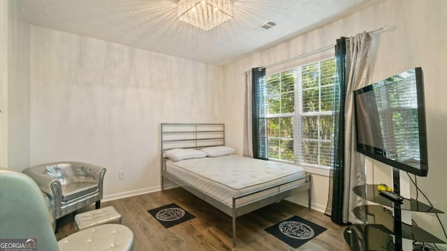 bedroom featuring visible vents, a textured ceiling, wood finished floors, a chandelier, and baseboards