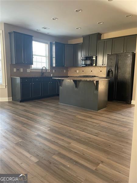 kitchen with tasteful backsplash, a kitchen island, a kitchen breakfast bar, black appliances, and dark wood-style flooring