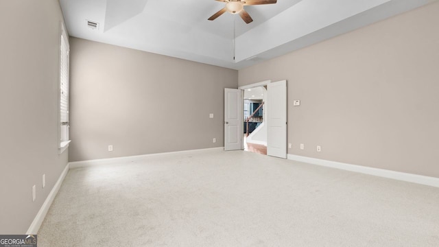 empty room with baseboards, light carpet, ceiling fan, and a tray ceiling