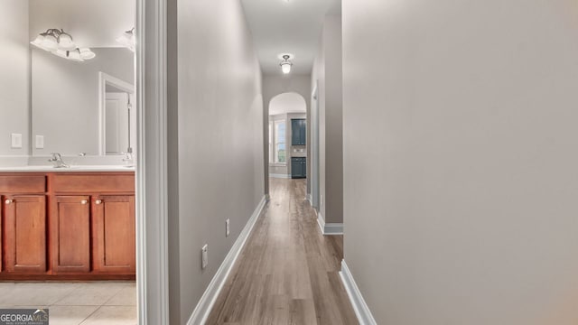 hallway featuring light wood finished floors, arched walkways, a sink, and baseboards