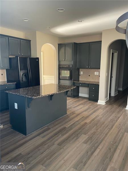 kitchen featuring dark stone counters, arched walkways, a kitchen island, and black appliances