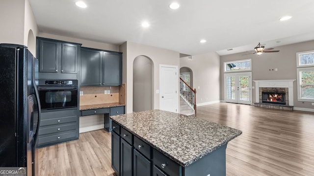kitchen with light wood finished floors, a center island, black appliances, a ceiling fan, and arched walkways
