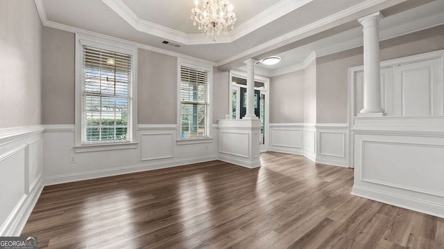 unfurnished dining area with a wainscoted wall, visible vents, ornate columns, ornamental molding, and wood finished floors