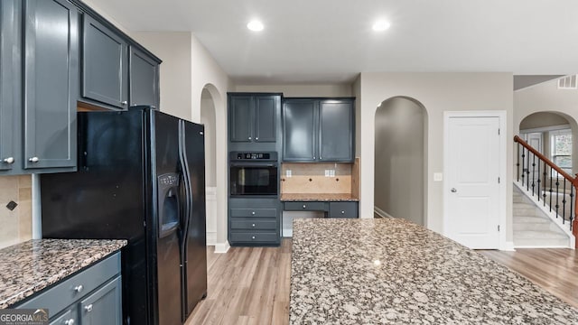 kitchen with decorative backsplash, light wood-type flooring, black appliances, light stone counters, and arched walkways