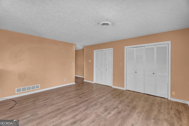 unfurnished bedroom with baseboards, visible vents, multiple closets, and wood finished floors