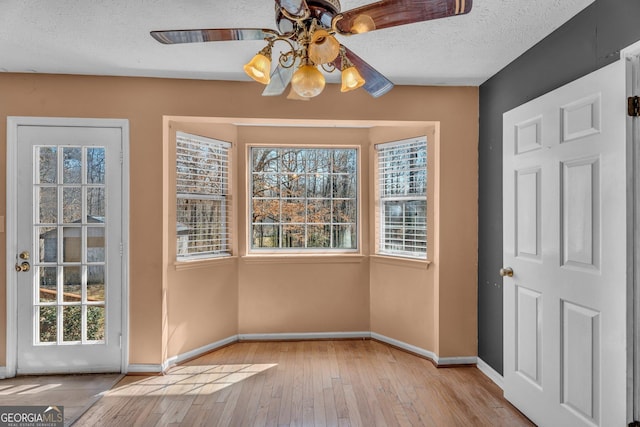 unfurnished dining area with a ceiling fan, a textured ceiling, baseboards, and hardwood / wood-style floors