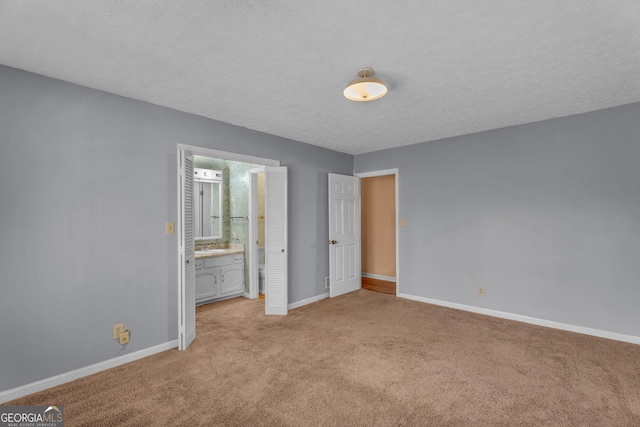 unfurnished bedroom with carpet floors, connected bathroom, a textured ceiling, and baseboards