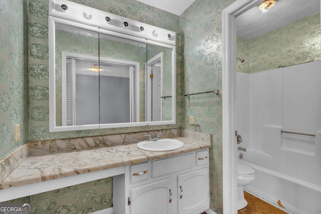 bathroom with a textured ceiling, toilet, shower / bath combination, vanity, and wallpapered walls