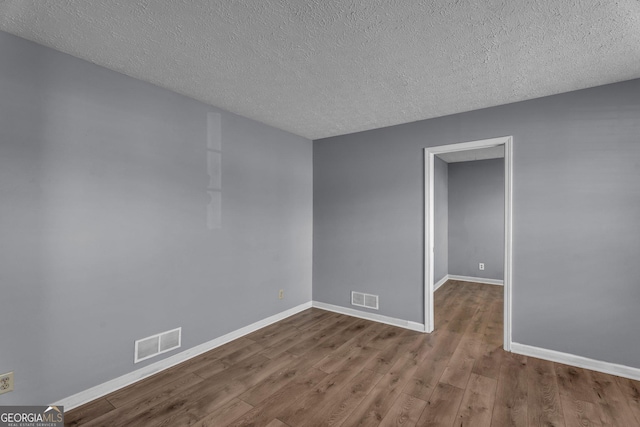 unfurnished room with a textured ceiling, wood finished floors, visible vents, and baseboards