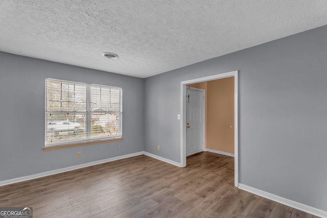 unfurnished room featuring a textured ceiling, wood finished floors, visible vents, and baseboards