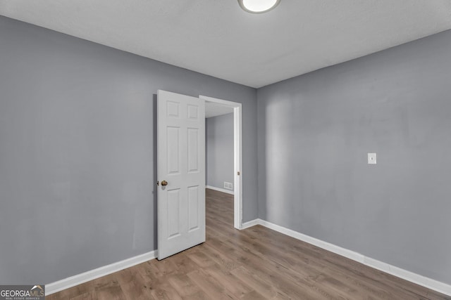 spare room with wood finished floors, visible vents, and baseboards