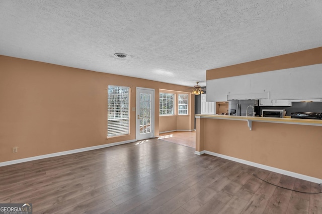 kitchen with baseboards, visible vents, a ceiling fan, a breakfast bar, and wood finished floors