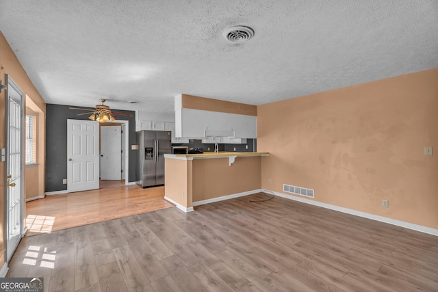 kitchen with a peninsula, stainless steel fridge, visible vents, and white cabinets