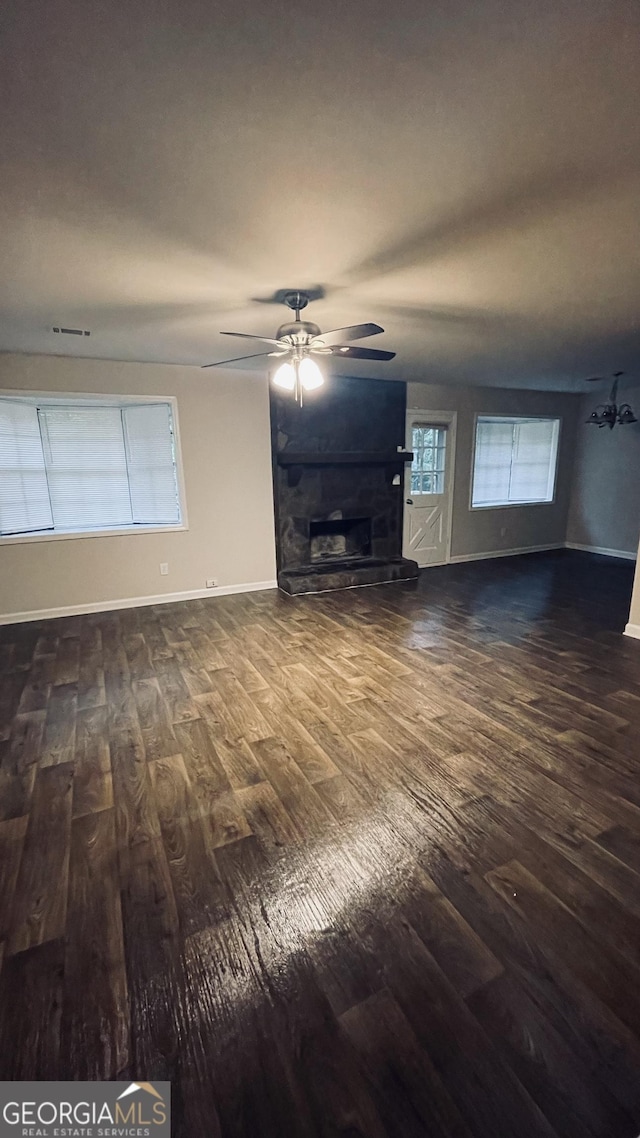 unfurnished living room with a fireplace with raised hearth, dark wood finished floors, baseboards, and ceiling fan