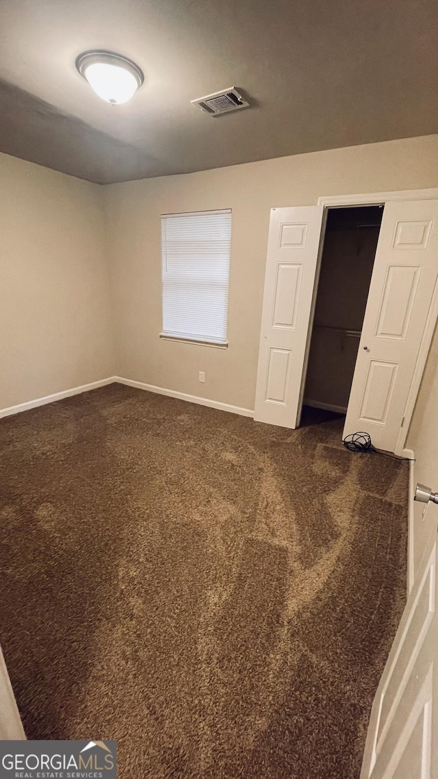 unfurnished bedroom with a closet, visible vents, dark carpet, and baseboards