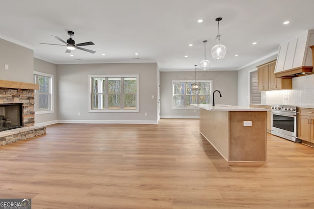 kitchen featuring a center island with sink, light countertops, decorative backsplash, a stone fireplace, and high end stove