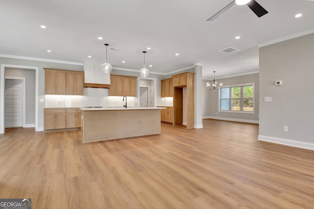 kitchen with a center island with sink, visible vents, light wood-style flooring, decorative backsplash, and ceiling fan with notable chandelier