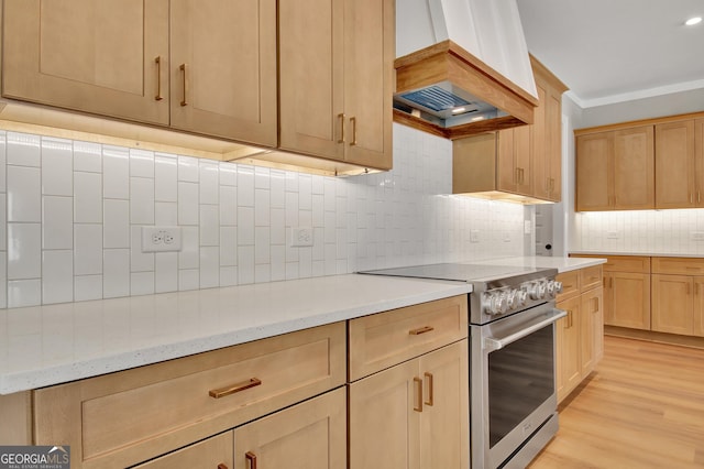 kitchen featuring tasteful backsplash, high end stainless steel range, light brown cabinetry, light wood-type flooring, and premium range hood