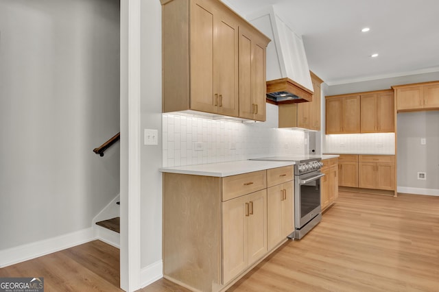 kitchen with light wood finished floors, high end range, light countertops, light brown cabinets, and backsplash