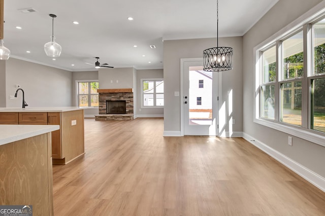 kitchen featuring crown molding, light countertops, a sink, a stone fireplace, and light wood-type flooring