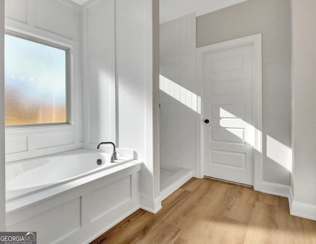 full bathroom featuring a garden tub, baseboards, wood finished floors, and a tile shower